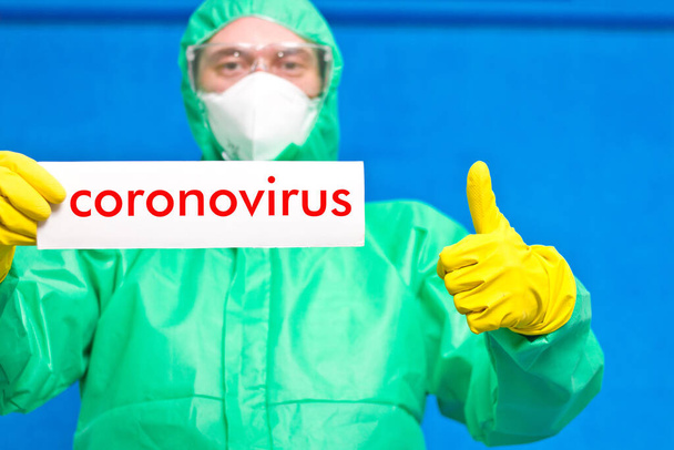 Orvosi dolgozó kezében egy fehér poszter a felirat coronavirus, álló kék alapon. - Fotó, kép