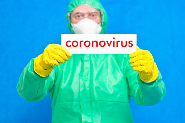 Orvosi dolgozó kezében egy fehér poszter a felirat coronavirus, álló kék alapon. - Fotó, kép