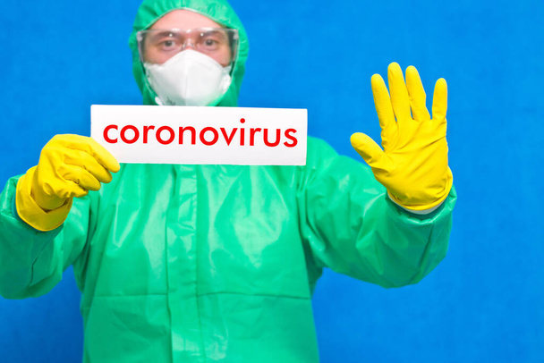 Üzerinde mavi arka planda duran beyaz bir afiş taşıyan Coronavirus yazan bir sağlık görevlisi.. - Fotoğraf, Görsel