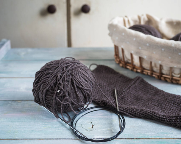 Ruční pletení z hnědé bavlněné příze, koš s přízí a kruhovými jehlicemi na dřevěném stole, výroba pletených oděvů - Fotografie, Obrázek