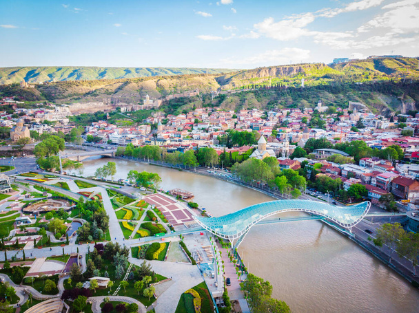 Ειρηνευτική γέφυρα και η παλιά πόλη της Τιφλίδας από εναέρια άποψη κατά τη διάρκεια της ανατολής. Αξιοθέατα και νέα τουριστική σεζόν στο Σακαρτβέλο. Τζόρτζια. 20204 - Φωτογραφία, εικόνα