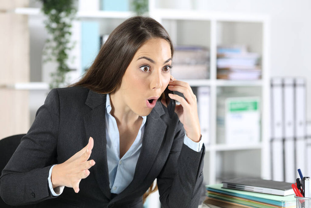 Sorpresa donna esecutiva che chiama sullo smart phone seduto su una scrivania in ufficio
 - Foto, immagini