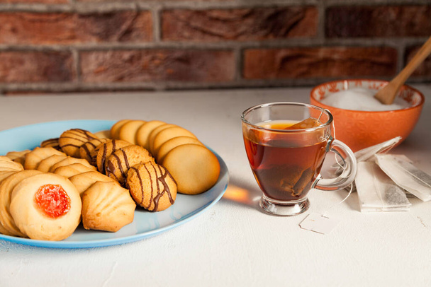 Mavi bir tabakta çeşitli çaydanlıklar, çay fincanı, şeker kasesi ve çay poşetleri beyaz bir masada ve tuğla arka planda. - Fotoğraf, Görsel
