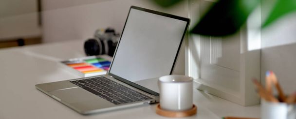 Обрезанный снимок дизайнерского стола домашнего офиса с макетом ноутбука, чашки, камеры, принадлежностей и украшений
 - Фото, изображение
