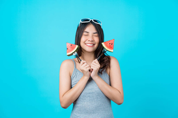 Portrait Attractive Asian young woman holding two Pieces of watermelon and wearing fashion sunglasses on isolated blue color background, copy space and studio, diet and healthy fruit concept - Photo, Image