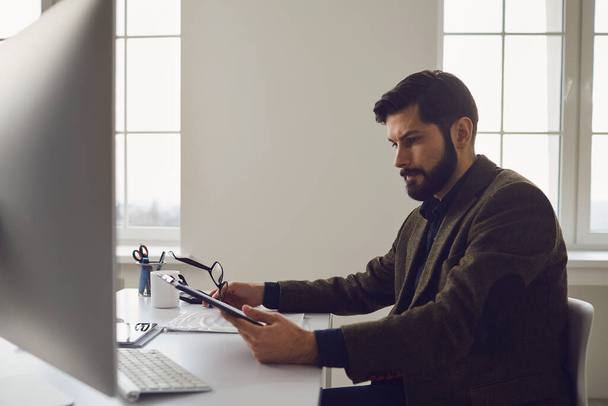 Бізнесмен працівник з бородою працює в комп'ютері за робочим місцем в офісі
. - Фото, зображення