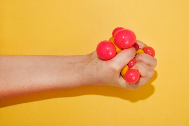 Hand squishing a colorful toy ball belonging to a child over a bright yellow background with shadow and copy space - Fotó, kép