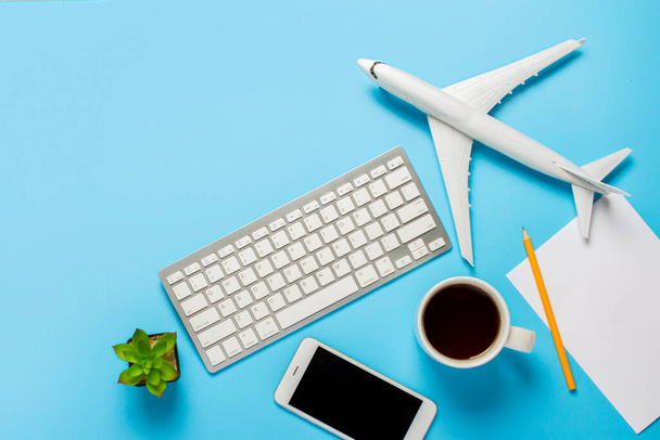 キーボード、花、飛行機、紅茶やコーヒーとカップ、青い背景に空白のシートと鉛筆。旅行計画の概念は、航空券をオンラインで購入し、航空券を販売する。バナーだ。フラットレイアウト、トップビュー. - 写真・画像