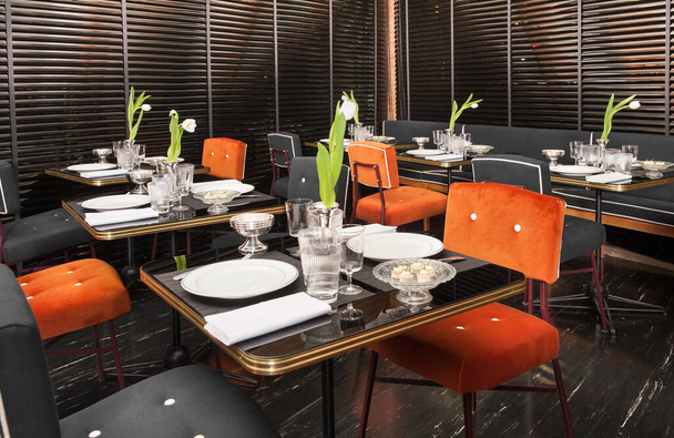 Interior de restaurante de lujo de los años 50 con acentos rojos y decoración negra con mesas para cenar con centros de flores
 - Foto, Imagen