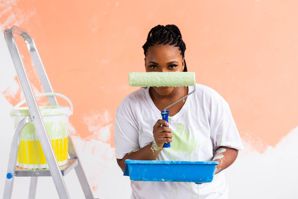 Boldog mosolygós afro-amerikai nő festészet belső fal az új ház. Újjáépítés, felújítás, lakásjavítás és felújítás koncepciója. - Fotó, kép
