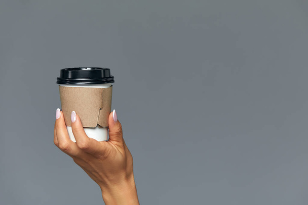 Рука девушки с бумажной чашкой кофе, серый фон Доброе утро, концепция. Пустое место для надписи
. - Фото, изображение