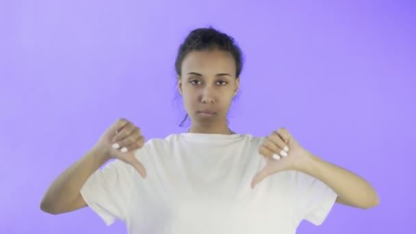 Hermosa joven con una camiseta blanca muestra el pulgar hacia abajo con ambas manos sobre fondo violeta
 - Imágenes, Vídeo