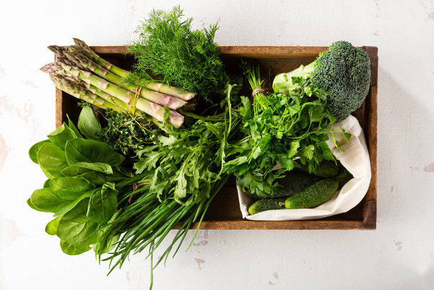 Fresh green vegetable and herbs in wooden crate on light surface - Fotografie, Obrázek