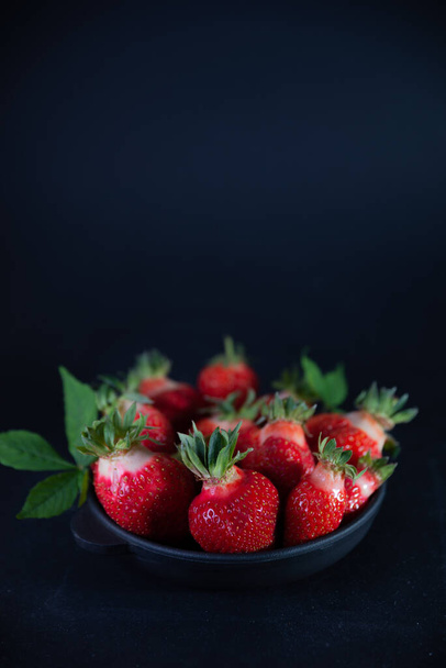 Fresh juicy strawberries in a black plate on a black matte background - Foto, Imagen