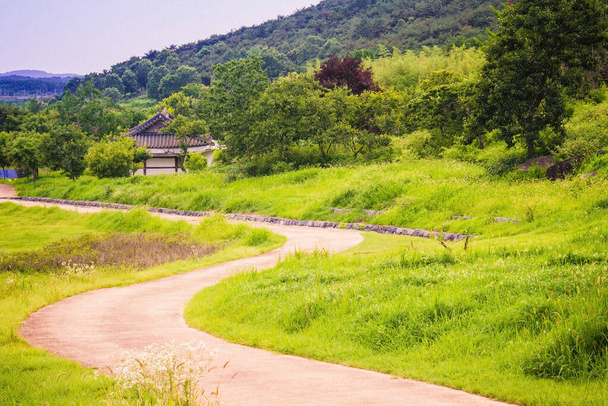 Droga biegnie w oddali. Wieś, wioska. Away to tradycyjny koreański dom. Wokół zielonych wzgórz. Letni dzień. - Zdjęcie, obraz