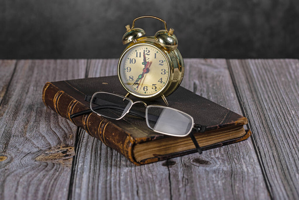 A book, reading glasses, and a watch. The concept of home recreation. Self-isolation of the house. - Фото, изображение