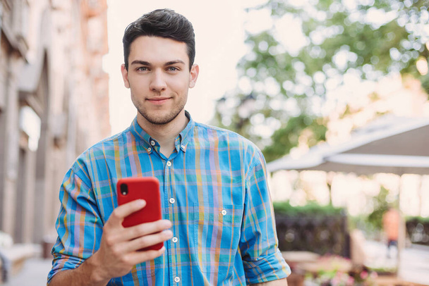 Young handsome business man using smartphone in a city. Cheerful men holding mobile phone. Technology, connection, communication, social media, fun, good news, relaxation, leisure concept - Fotó, kép