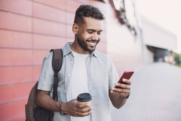 Young handsome men using smartphone in a city. Smiling student man texting on his mobile phone. Coffee break. Modern lifestyle, connection, business concept - Photo, image