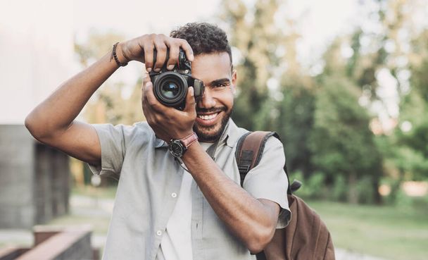 Young man photographer takes photographs with dslr camera in a city. Travel, vacations, professional freelance work and active lifestyle concept - Foto, Imagen