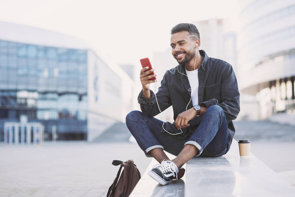 Young handsome men using smartphone in a city. Smiling student man texting on his mobile phone. Coffee break. Modern lifestyle, connection, business concept - Photo, Image