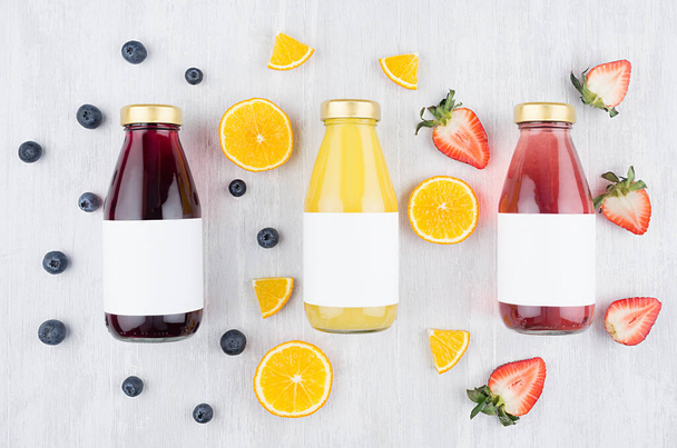Fresh yellow orange, pink strawberry, violet blueberry juices in glass bottles with blank label on white wood board, mock up for design, advertising. - Foto, Imagen