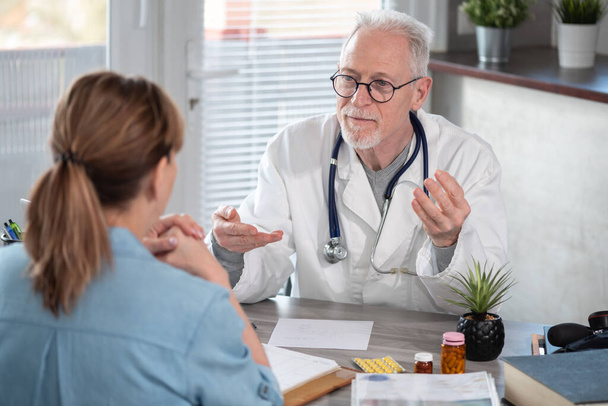 Oberarzt diskutiert mit Patientin in Arztpraxis - Foto, Bild