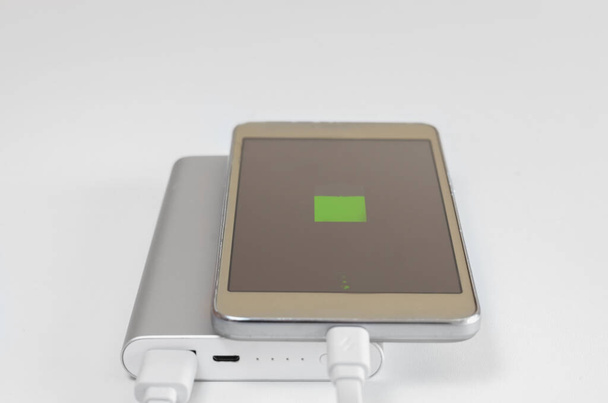 白い背景にパワーバンクから充電スマートフォンのバッテリーを充電する兆候が表示されます。旅行のための充電デバイスのための外部ソリューション . - 写真・画像