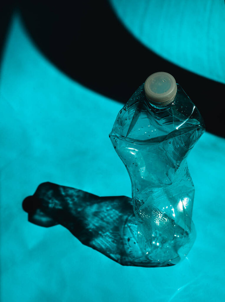 Zgnieciona pusta plastikowa butelka PVC na niebieskim tle. Koncepcja zanieczyszczenia tworzyw sztucznych. Plastik jednorazowego użytku jest uzależnieniem człowieka, które niszczy naszą planetę i wpływa na nasze wody, życie morskie  - Zdjęcie, obraz