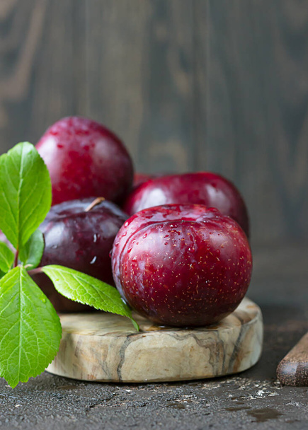 Fresh purple plums with leaves on wooden cutting board. Autumn harvest. Dark brown concrete background. - Zdjęcie, obraz