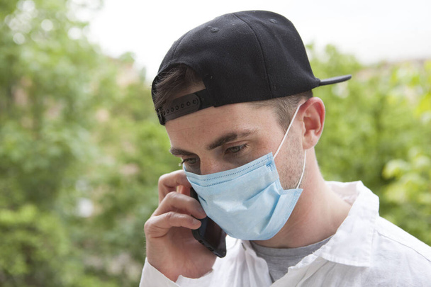 Młody człowiek odbiera złe wieści przez telefon, nosi ochronną maskę medyczną. Zdenerwowany mężczyzna rozmawiający przez telefon podczas izolacji koronawirusów - Zdjęcie, obraz