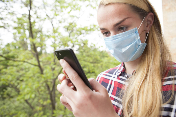 Mujer joven con máscara médica al aire libre, usando su teléfono inteligente. Redes sociales, concepto de aplicaciones móviles
 - Foto, imagen