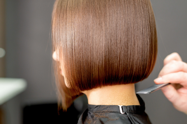Vista posterior de la mano del peluquero peinando pelo corto de la mujer en el salón de peinado
. - Foto, Imagen