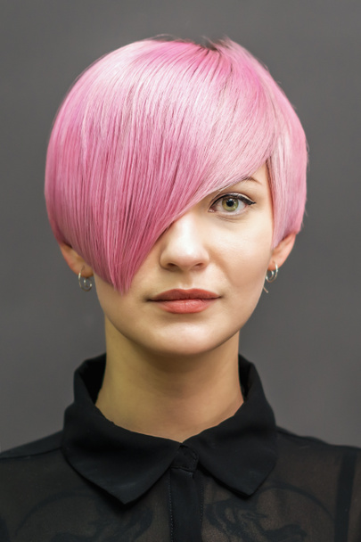 Πορτρέτο της όμορφης νεαρής γυναίκας με ροζ κοντά μαλλιά σε σκούρο γκρι φόντο. - Φωτογραφία, εικόνα