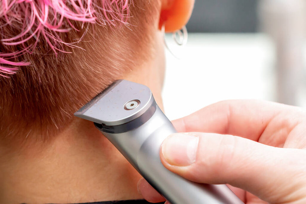 Visão traseira cabeleireiro mão está raspando o cabelo rosa da mulher com aparador elétrico no salão de cabeleireiro, close-up
. - Foto, Imagem
