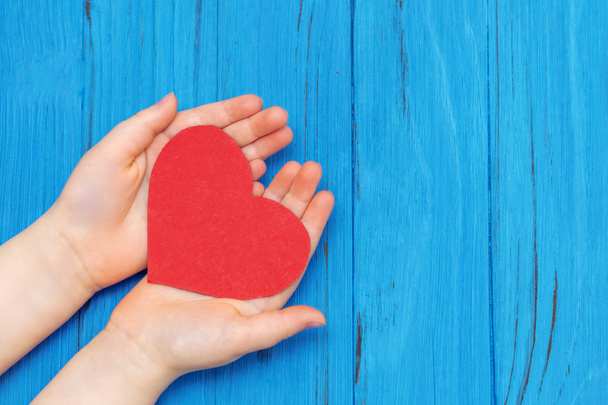 Red heart on the child's hands on wooden background. Healthcare medical concept. Copy space. - Photo, Image