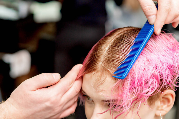 Nahaufnahme der Hände des Friseurs, der im Friseursalon die rosafarbenen Haare einer jungen Frau durch Kamm trennt. - Foto, Bild