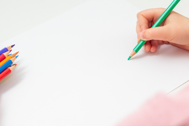 Children's hand with a green color pencil on a white background. The hand of child drawing on a sheet with a green pencil. Mockup. Copy space. - 写真・画像