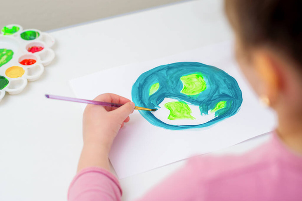 女の子のバックビューは、紙の上にブラシで惑星の地球を描いている。地球の日の概念. - 写真・画像