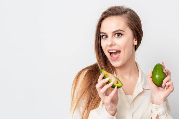 Portrait of pleasantly surprised woman with a two avocado on white background. - Photo, Image