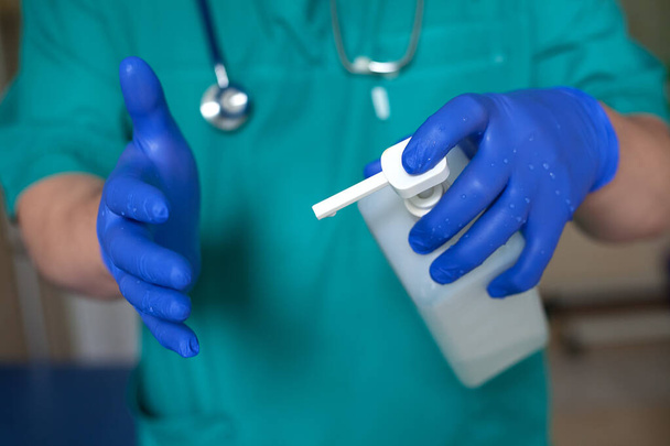 O médico esfrega as mãos com um anti-séptico. Nas mãos estão usando luvas azuis. O médico de fato verde. Foco local
 - Foto, Imagem