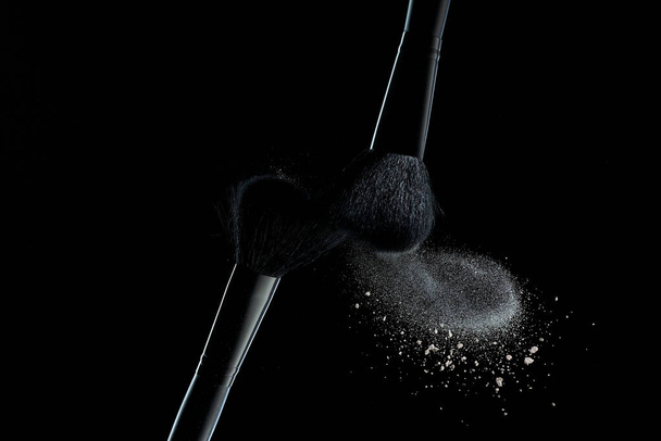 Makeup brushes with colorful powder explosion on black background. High speed photography of cosmetics. - Foto, Imagem