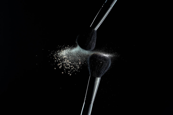 Makeup brushes with colorful powder explosion on black background. High speed photography of cosmetics. - Fotografie, Obrázek