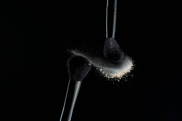 Makeup brushes with colorful powder explosion on black background. High speed photography of cosmetics. - Foto, imagen