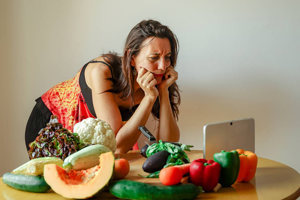 Nainen käyttää taulutietokonetta keittiössä kokkaamiseen. Nainen etsii hedelmiä resepti. Keittiö nainen tekee terveellistä ruokaa tabletti tietokone. Keskity kasvoihin- Kuva
 - Valokuva, kuva