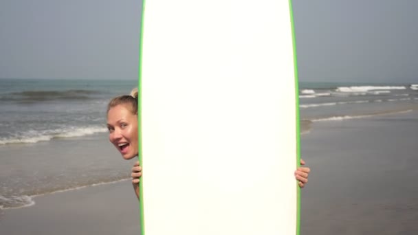 Uma mulher alegre espreita por trás de uma prancha de surf e mostra sua língua
 - Filmagem, Vídeo