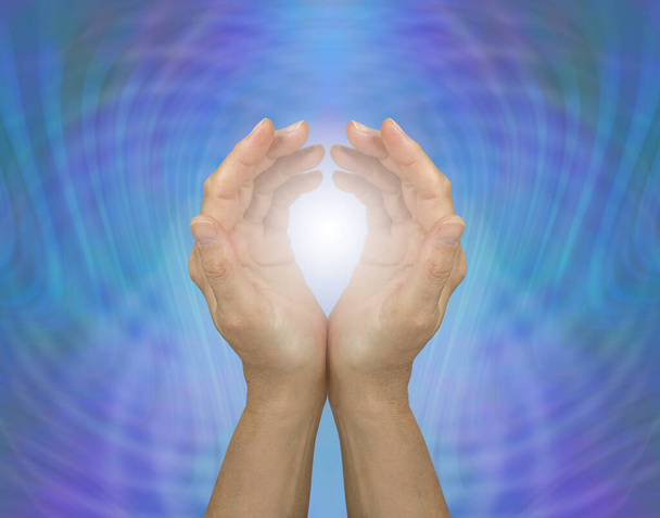 Pulsoiva kvanttiparantava energia - kuppaantuneet naisen kädet, jotka peittävät valkoisen parantavan valon sinistä vihreää energiamatriisitaustaa vasten  - Valokuva, kuva