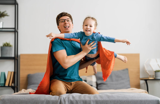 Father and his child playing together. Girl and dad in Superhero costume. Daddy and kid having fun, smiling and hugging. Family holiday and togetherness. - Foto, afbeelding
