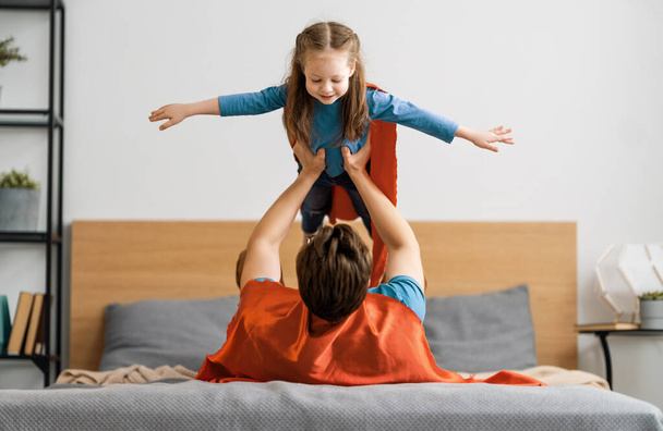 Father and his child playing together. Girl and dad in Superhero costume. Daddy and kid having fun, smiling and hugging. Family holiday and togetherness. - Zdjęcie, obraz