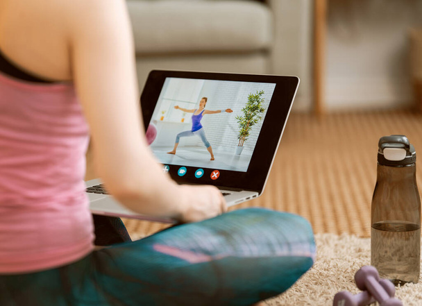 Νεαρή γυναίκα σε activewear βλέποντας online μαθήματα σε φορητό υπολογιστή, ενώ η άσκηση στο σπίτι. - Φωτογραφία, εικόνα