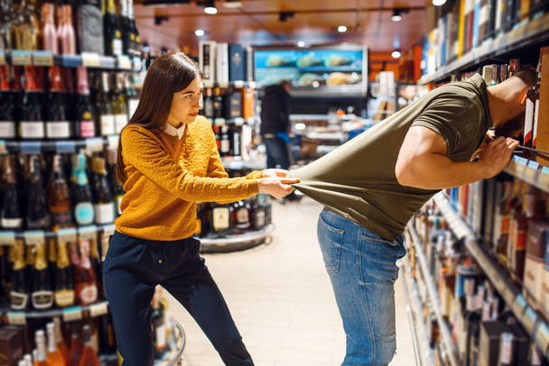 Funny couple choosing alcohol in grocery store. Man and woman with cart buying beverages in market, customers shopping food and drinks - Photo, Image